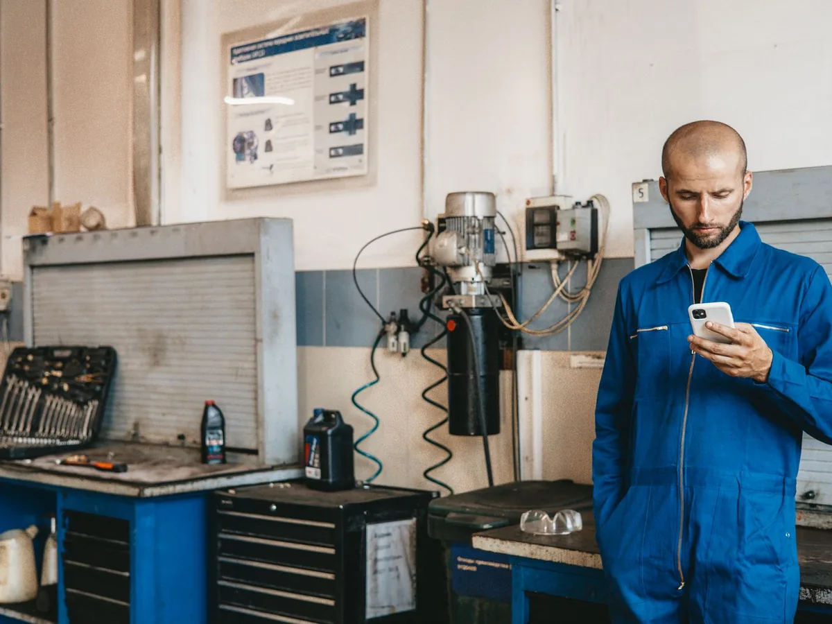 Un mécanicien en bleu de travail consulte son téléphone dans son atelier