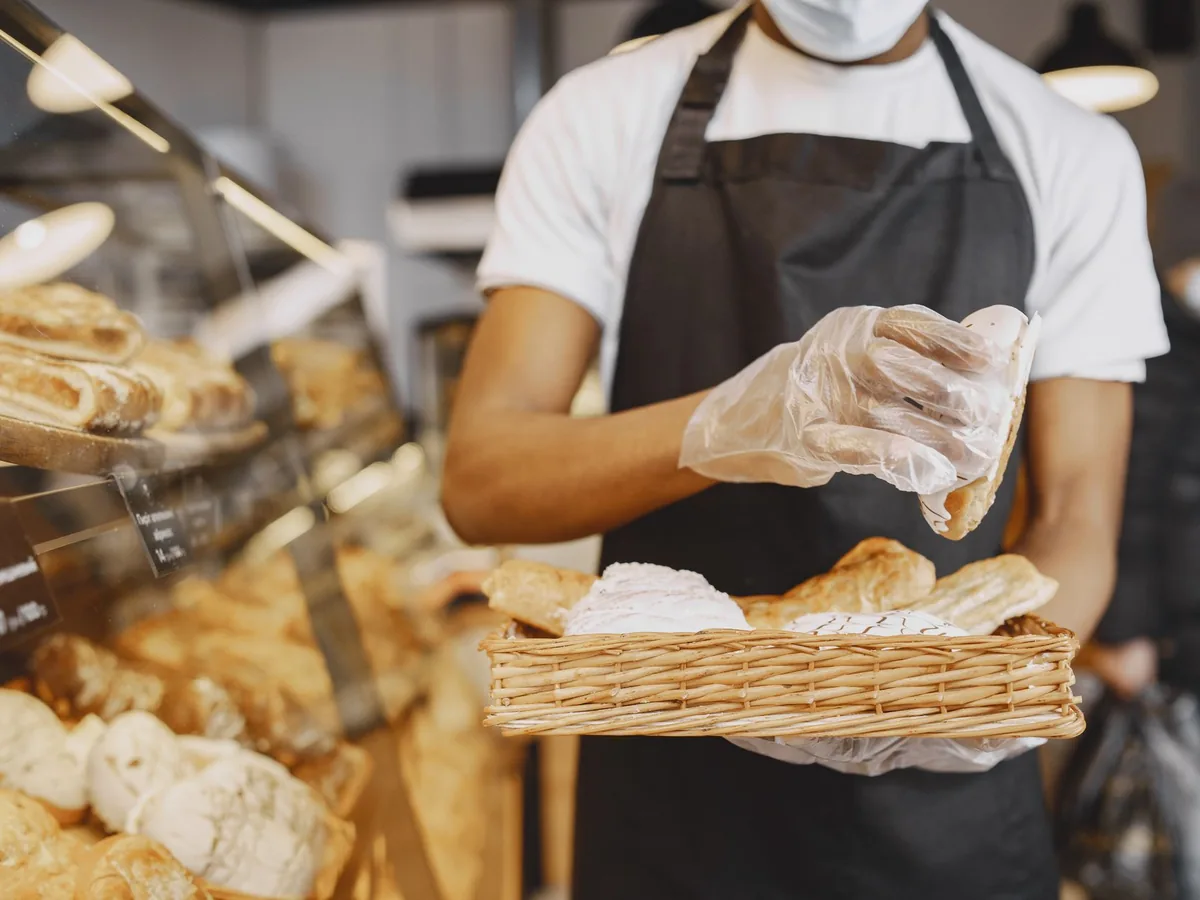 Un boulanger derrière son comptoir consulte son smartphone pendant que des clients attendent devant l'étal de pain.
