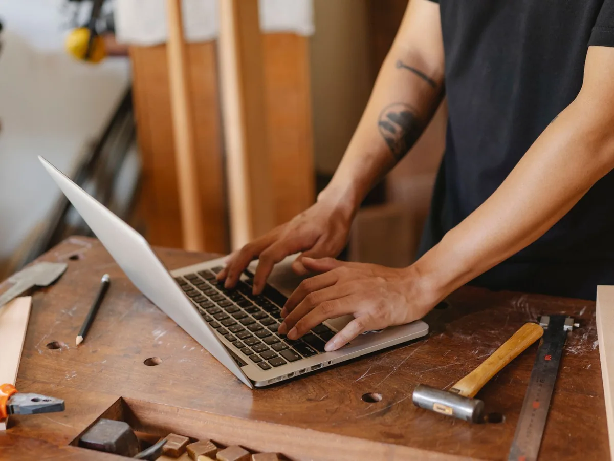 Un menuisier dans son atelier utilisant un smartphone pour consulter son site web professionnel, étabrissements de menuiserie en arrière-plan.