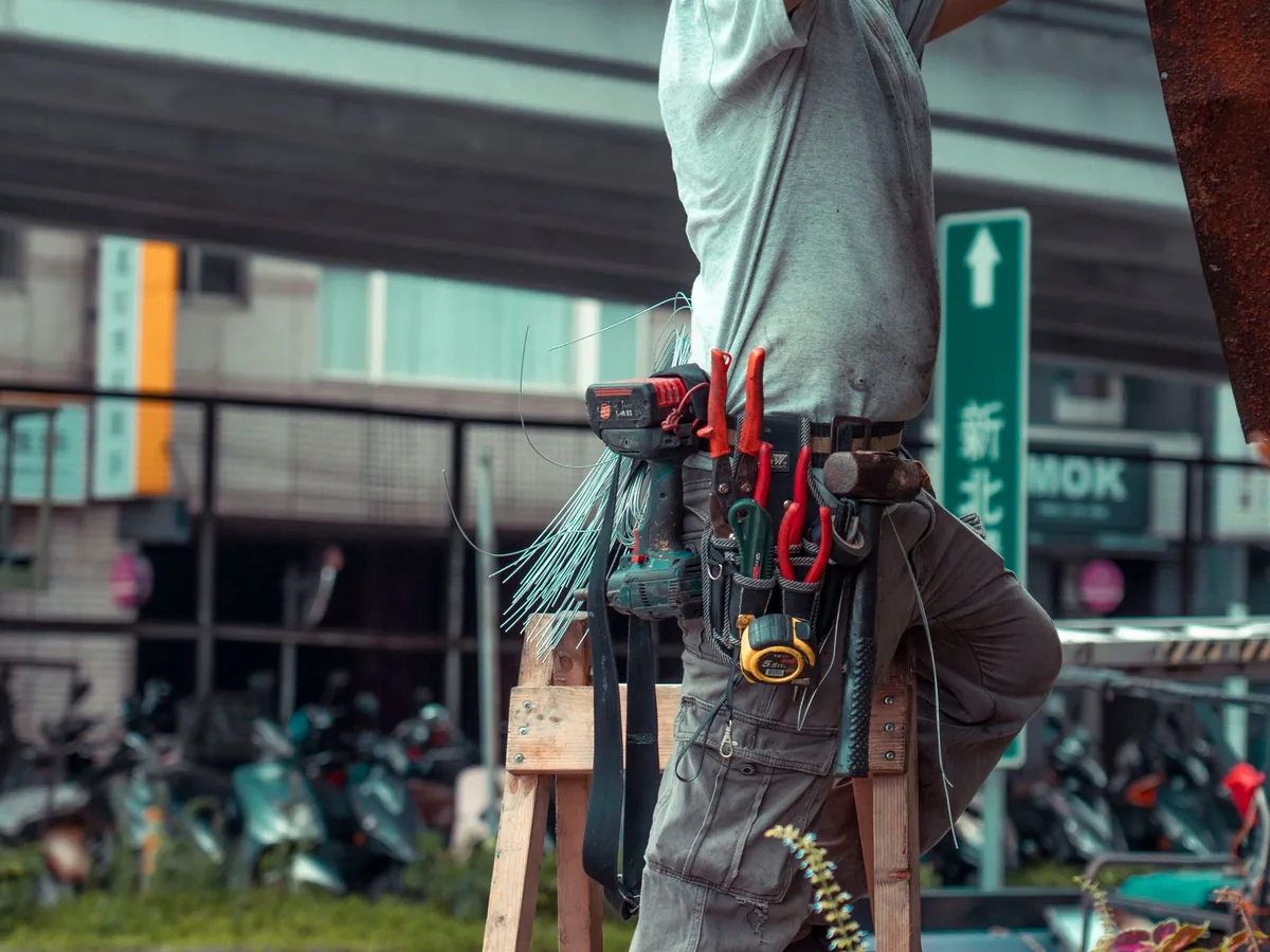Un plombier rédige un devis sur son smartphone dans la cour d'un chantier de rénovation de salle de bain.