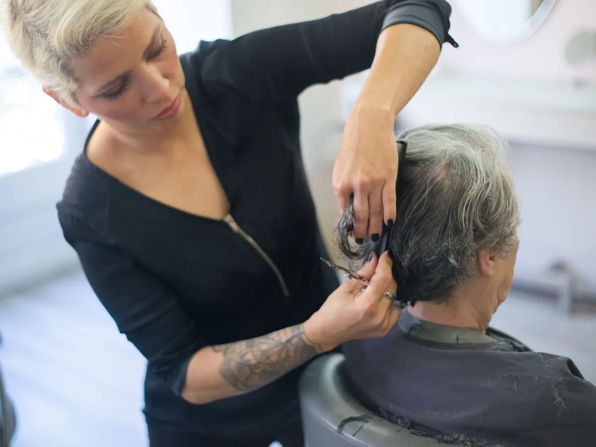 Un coiffeur dans son salon présente un devis écrit à sa cliente avant de commencer une coloration.