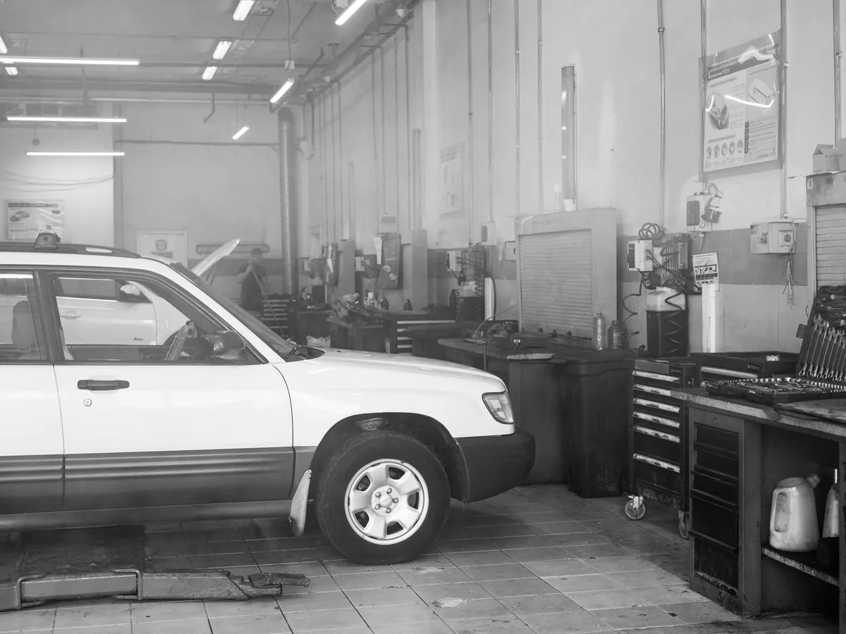 Un garagiste dans son atelier présente un devis écrit à un client à proximité d'une voiture sur un pont élévateur.
