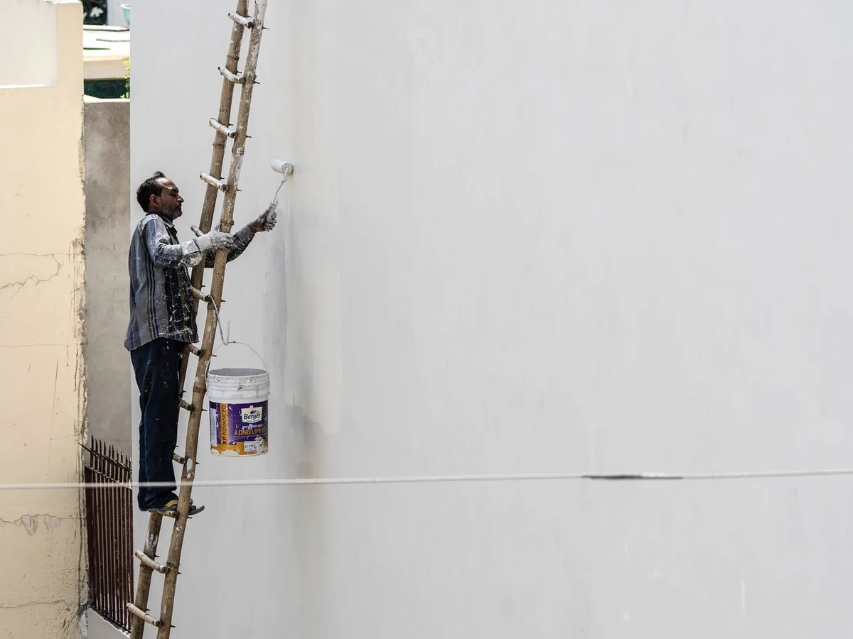 Un artisan peintre en bâtiment prépare un devis sur un ordinateur portable dans son atelier, à côté de pots de peinture et de nuanciers.