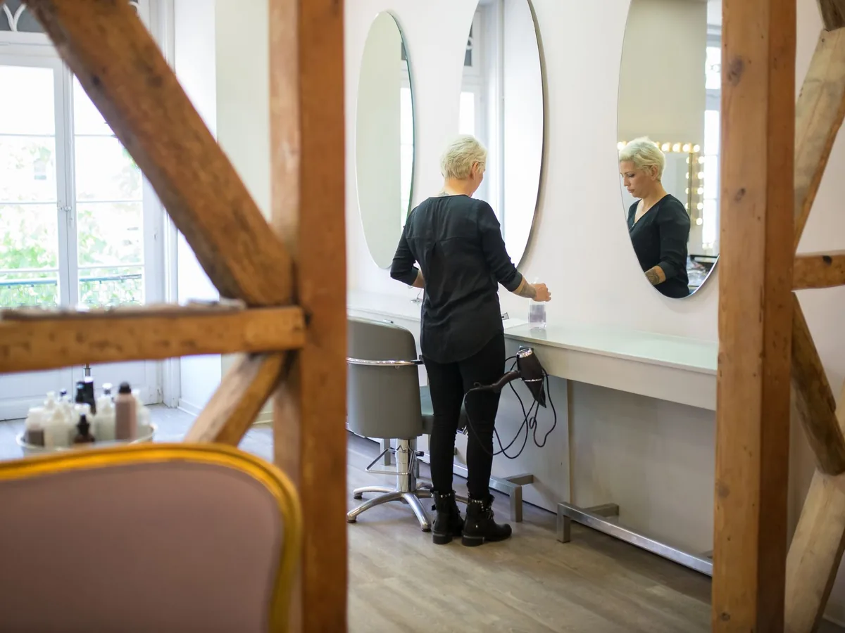 Coiffeuse consultant son agenda de rendez-vous en ligne sur une tablette dans son salon.