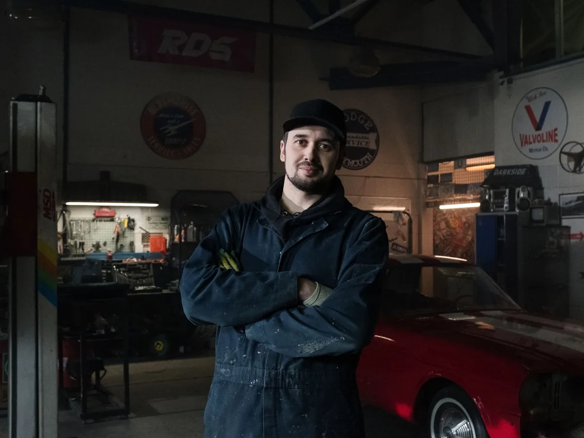Un client consulte son téléphone pour choisir un créneau de rendez-vous dans un garage automobile, le capot d'une voiture ouvert en arrière-plan.