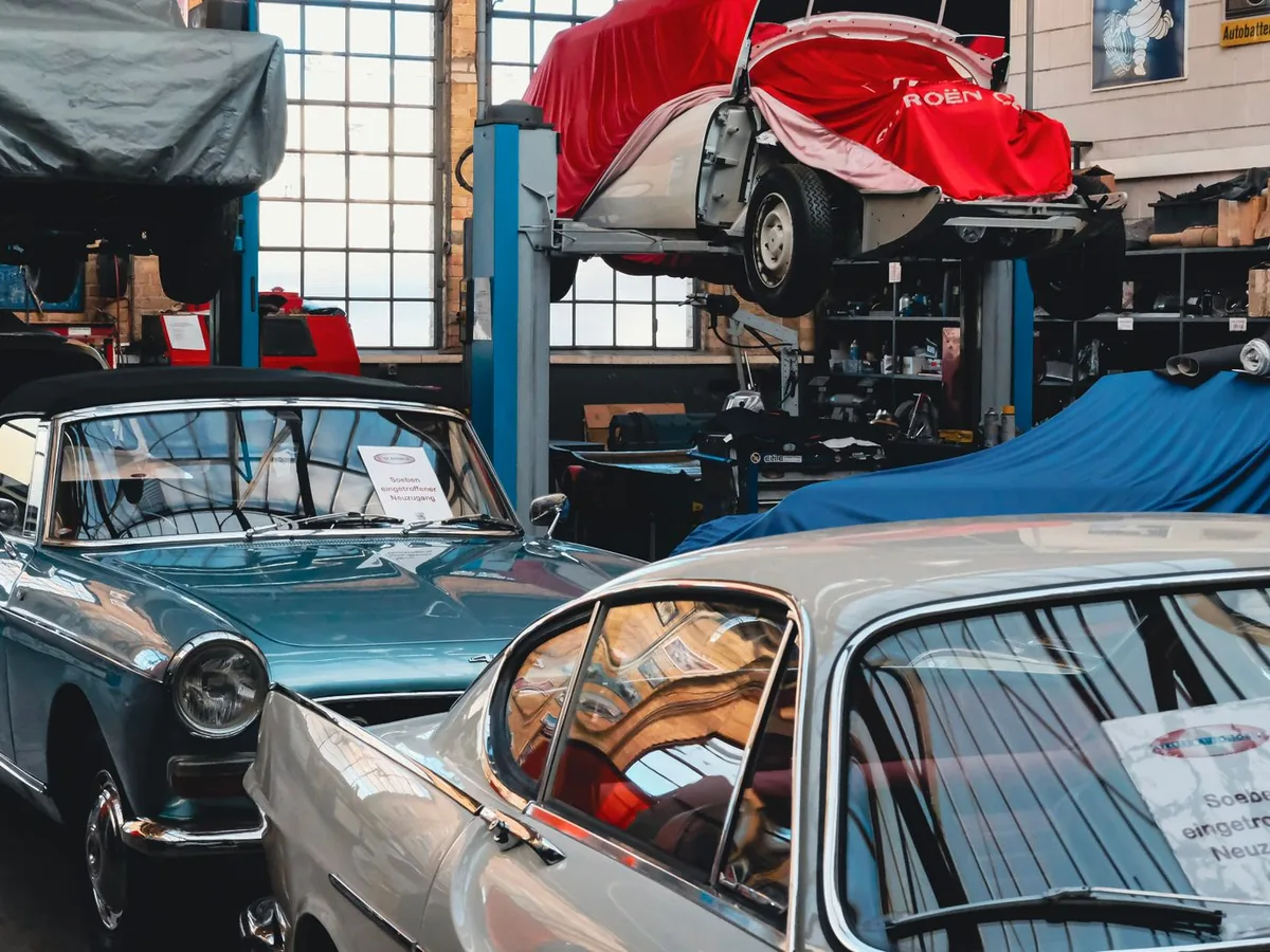 Un garagiste sur son smartphone devant son atelier, la porte ouverte du garage automobile en arrière-plan